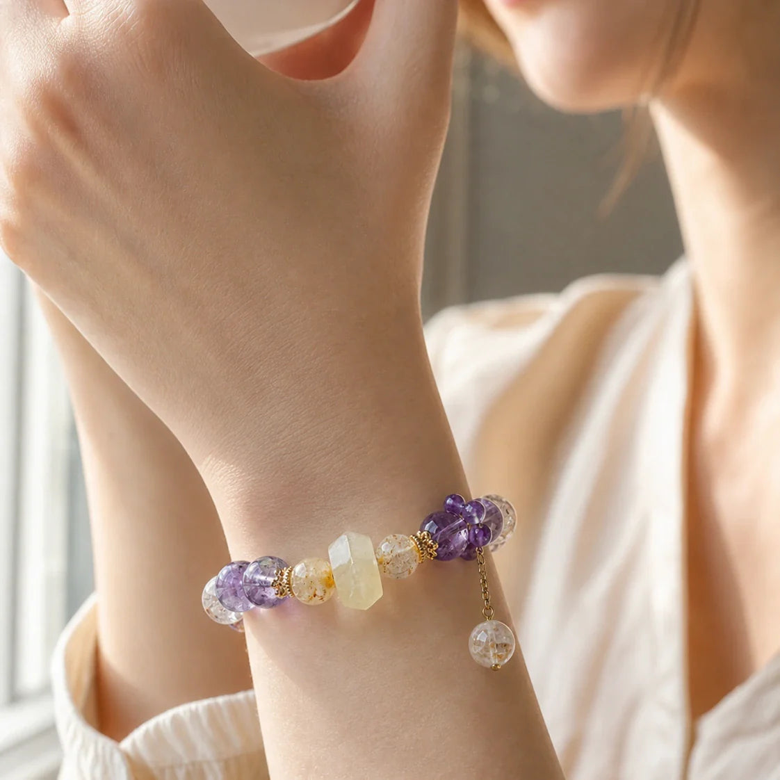 Natural amethyst and rutilated quartz bracelet worn beside a sunlit window